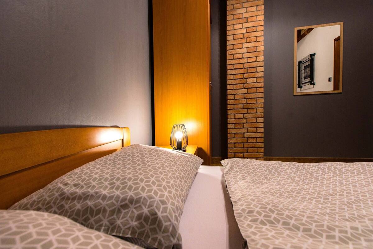 Ein Hotelzimmer mit zwei Betten, einem Holzkopfteil, einem Wandspiegel und einer Ziegelwand.