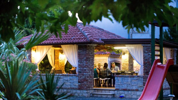 A stone building with a red-tiled roof, a patio area with chairs and a table, and a red slide. - Apartments Sanic 518 (Lopar)