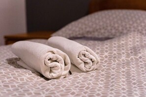 A neatly made bed with a patterned bedspread and two rolled towels placed on it.