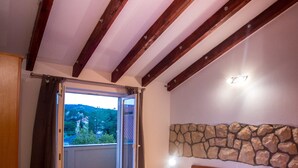 A bedroom with a wooden bed, a stone wall, and a balcony with a view of trees. - Apartments Sanic 518 (Lopar)