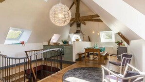Ein geräumiges Loft mit hoher Decke, freiliegenden Holzbalken, einer Essecke mit rundem Tisch und einer Küche mit modernem Herd.