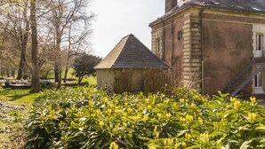 Ein traditionelles Steinhaus mit Satteldach und Schornsteinen, umgeben von einem gepflegten Garten mit blühenden Pflanzen.