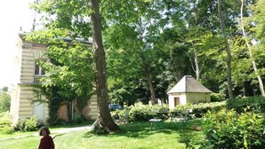 Ein Gebäude mit einem großen Baum davor, einer kleinen Struktur und einer Rasenfläche.