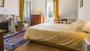 Ein Schlafzimmer mit einem Bett, einem Schminktisch, einem Sessel, einem Tisch, einer Lampe und einem Kamin.