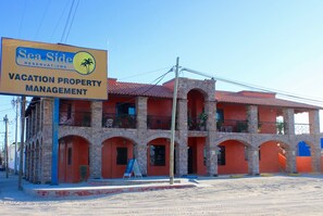 A multi-story building with a red-tiled roof and stone facade, featuring balconies and arched doorways. A signboard for 'Sea Side Reservations' is visible on the left. - Las Gaviotas 2BR 402 by Casago (Puerto Peñasco)
