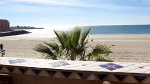 Une vue sur la plage avec un balcon carrelé, des palmiers et une côte lointaine.