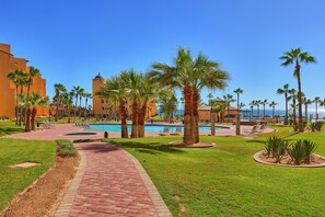 A resort pool area with palm trees, a clear blue sky, and a view of the ocean. - Princesa by Casago (Puerto Peñasco)