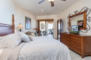 Une chambre avec un grand lit, une commode, un ventilateur de plafond et un balcon avec des chaises.