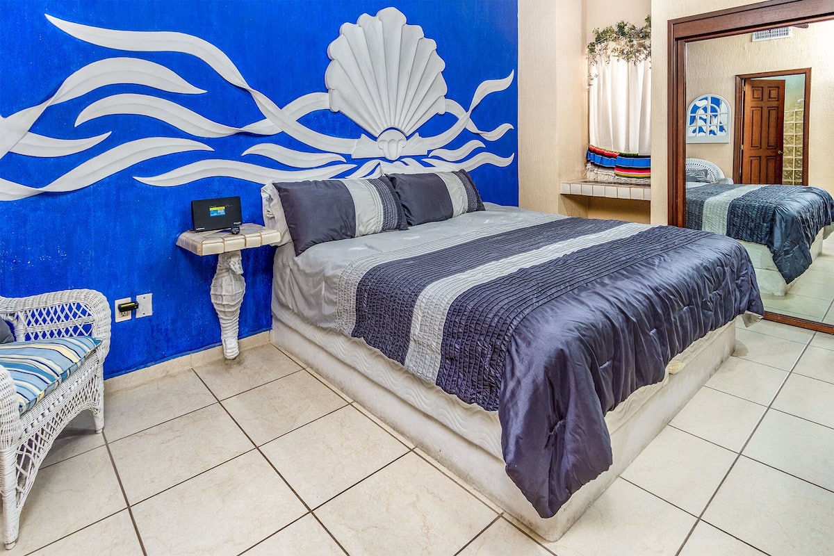 Ein Schlafzimmer mit Bett, Nachttisch, Sessel und Wand mit blau-weißem Dekor.