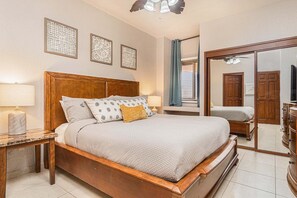 Ein Schlafzimmer mit einem hölzernen Bett, einem Nachttisch mit Lampe, einem Spiegel und einem Fenster mit Vorhängen.