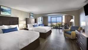 A hotel room with two beds, a desk, a chair, and a balcony with a view of the ocean. - Gorgeous Caravelle Resort Ocean View Double Efficiency (Myrtle Beach)