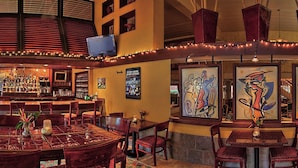 A bar area with a counter, chairs, and tables. There are framed artworks on the walls. - Gorgeous Caravelle Resort Ocean View Double Efficiency (Myrtle Beach)