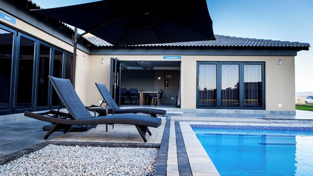 Une maison moderne dotée d’une piscine, de chaises longues et d’un patio couvert.
