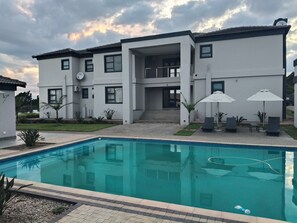 A modern two-story building with a swimming pool, outdoor seating, and a well-maintained garden. - Sagwadi Hotel (Bushbuckridge)