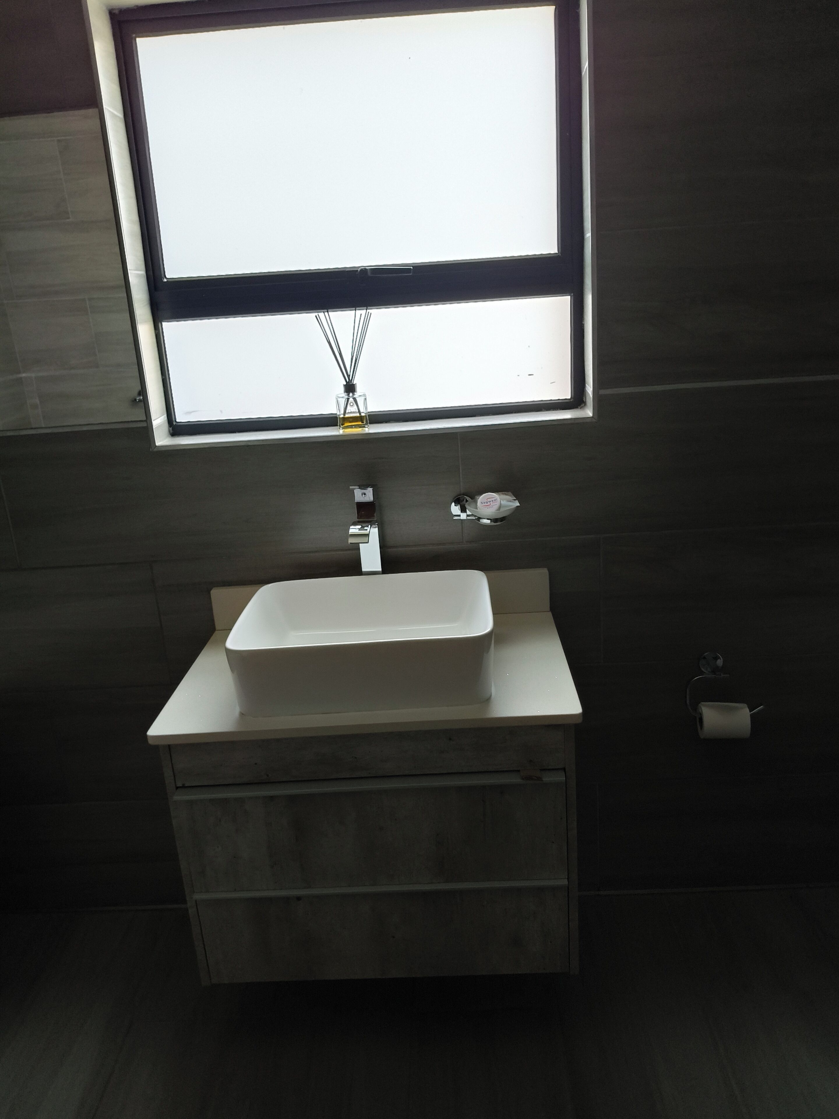 A bathroom with a white sink, a mirror, and a window above the mirror.