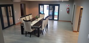 A dining area with a long table and chairs, a fire extinguisher on the wall, and a view of a swimming pool through glass doors. - Sagwadi Hotel (Bushbuckridge)