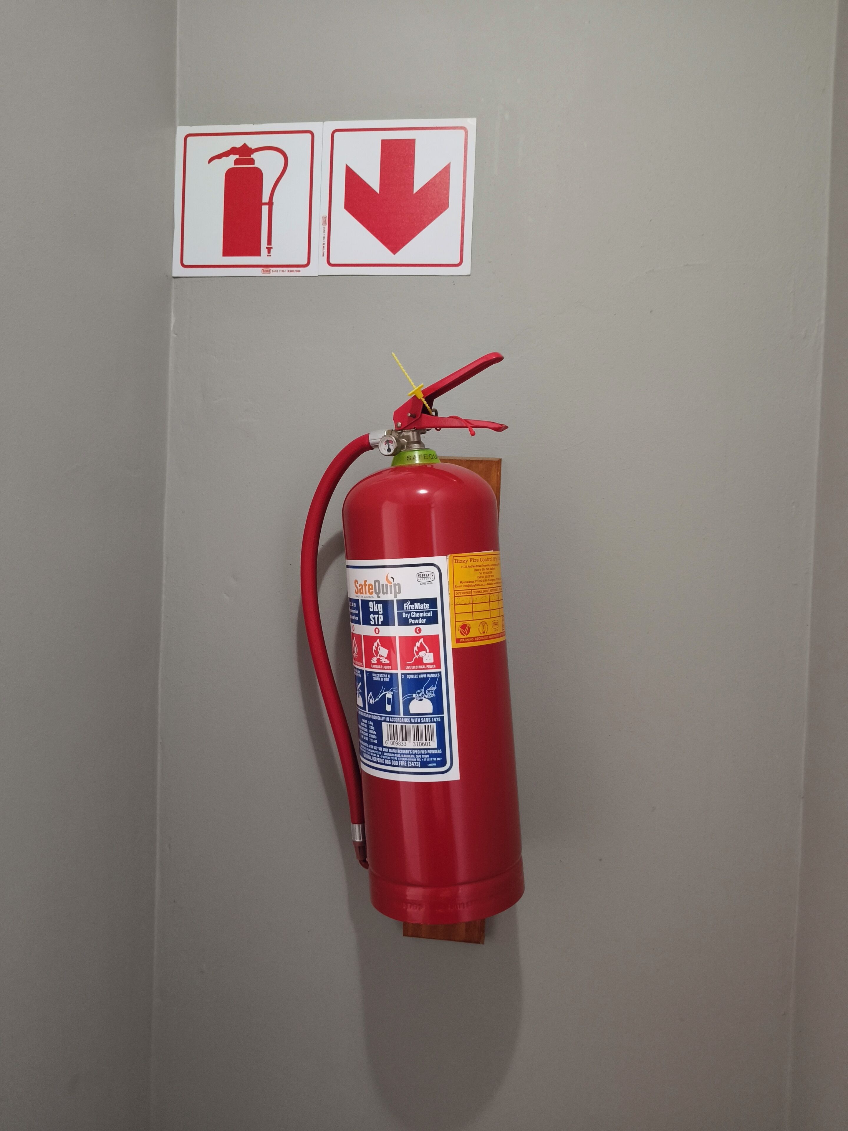 A red fire extinguisher mounted on a wall with two safety signs above it.