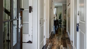 Een gang met houten vloeren, witte muren en een combinatie van open en gesloten deuren.