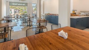 A modern dining area with wooden tables and chairs, a kitchen counter with food items, and a view of the outside through large windows. - Isola12 (Kas)