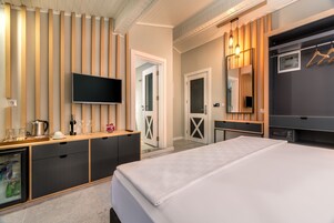 Quarto de hotel moderno com cama grande, televisão, minibar e parede revestida de madeira.