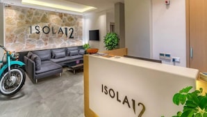 A modern reception area with a stone wall, a sofa, a motorcycle, and a reception desk labeled "ISOLA12". - Isola12 (Kas)