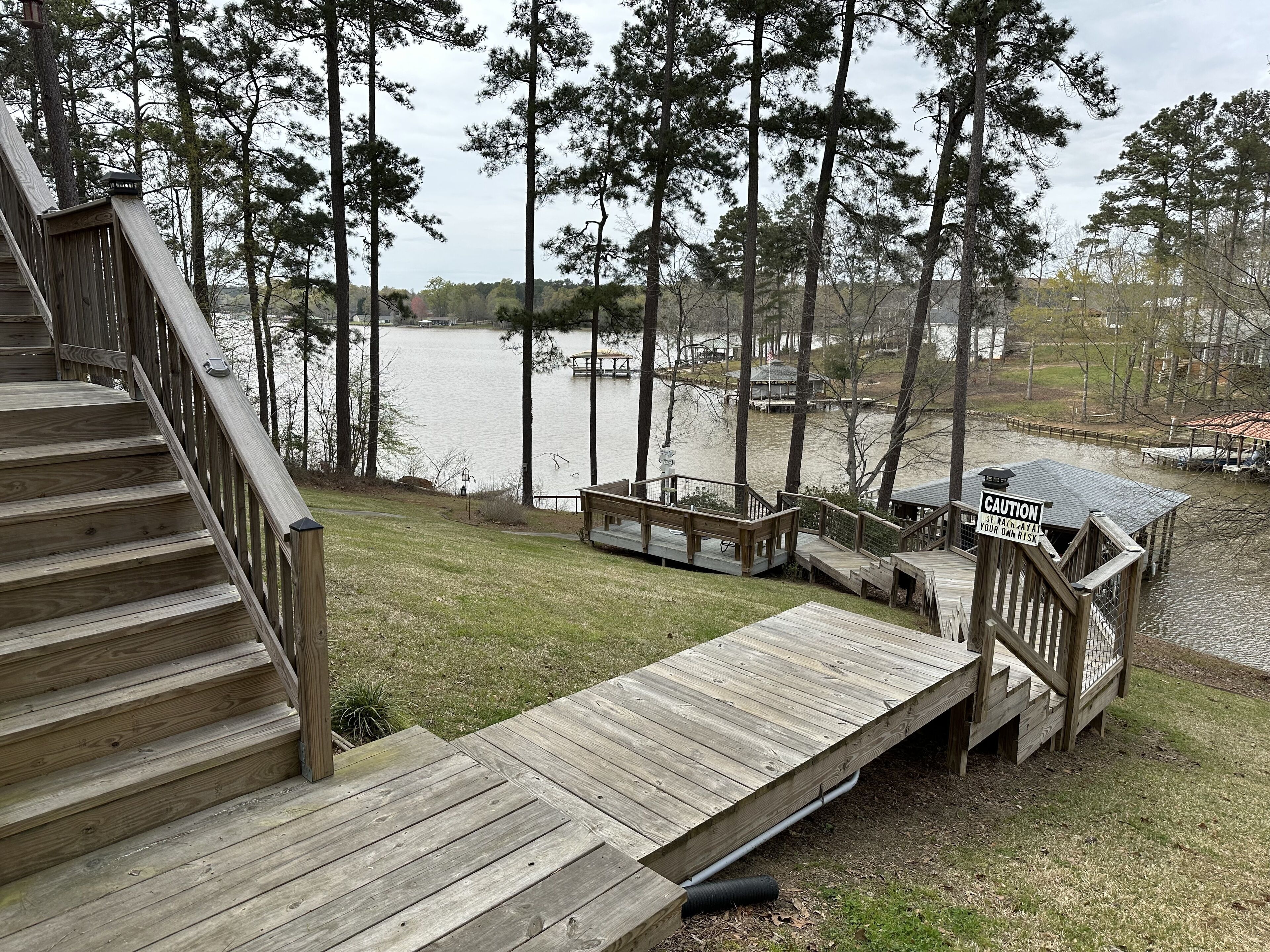 Une terrasse en bois avec un escalier menant à une jetée surplombant un lac, le tout entouré d’arbres.