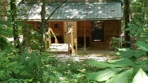 Eine rustikale Holzhütte mit geneigtem Dach, umgeben von dichtem Wald.