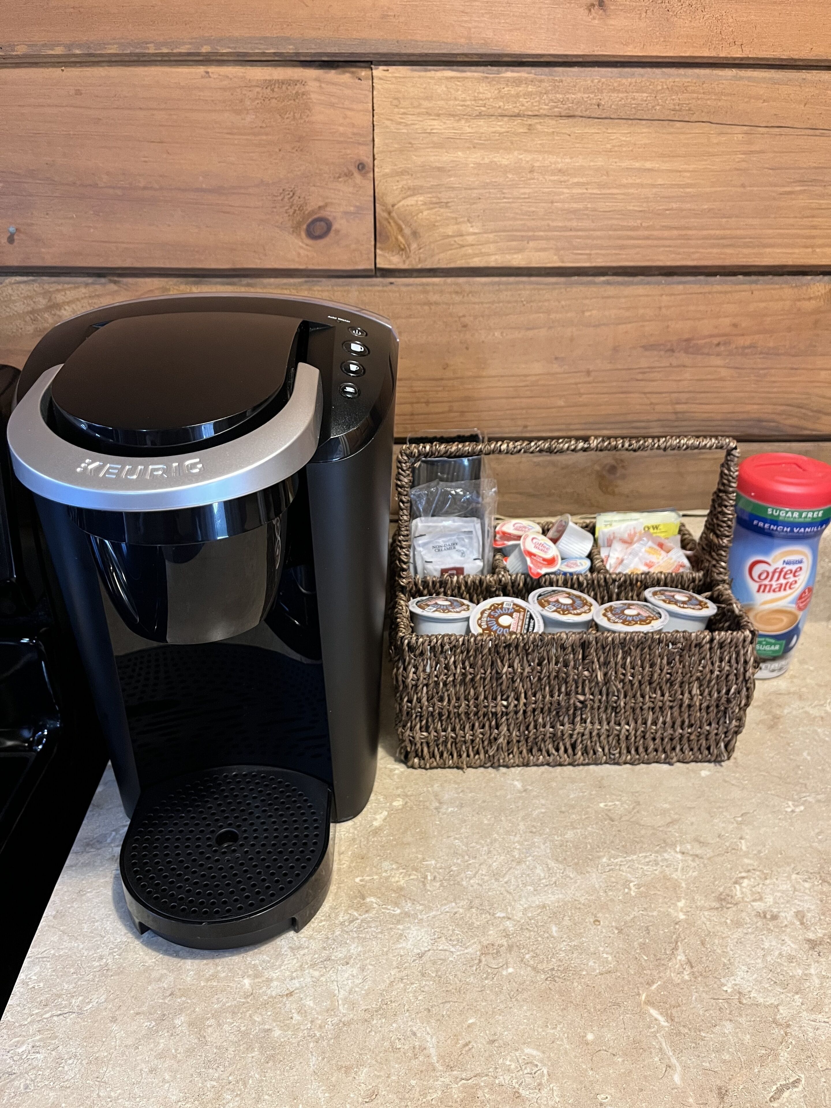 A Keurig coffee maker on a kitchen counter with a basket of coffee pods and a container of coffee creamer.