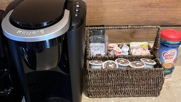 A Keurig coffee maker on a kitchen counter with a basket of coffee pods and a container of coffee creamer.