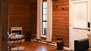 Ein Blockhaus-Interieur mit Holzwänden, einer Kandelaberleuchte, einer Tür, einem Fenster und einem Kamin.