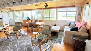 A spacious living area with a wooden ceiling, a dining table with chairs, a sofa, and a wicker basket. - Come Relax In This Spacious 3 Bedroom Cottage, Lake Views On Both Sides. (Colchester)