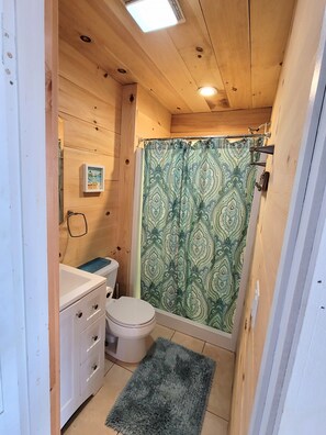 Un baño pequeño de madera con inodoro, lavamanos y cortina de ducha.