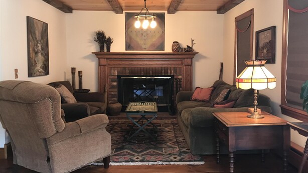A cozy living room with a fireplace, wooden furniture, and a chandelier. - Beautiful 4br home, village of Bolton Landing. Great location! Walk everywhere! (Bolton Landing)
