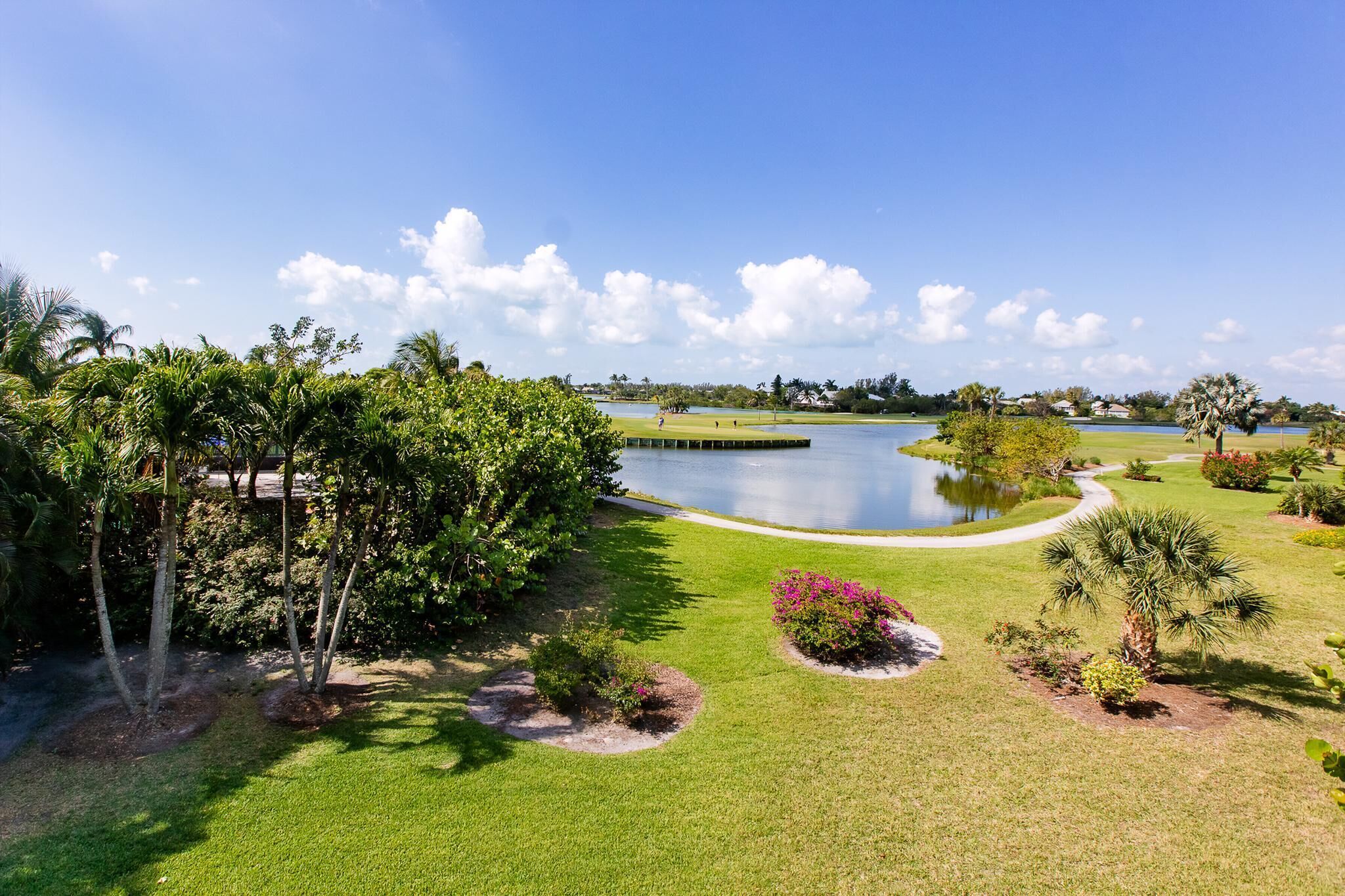 A well-maintained golf course with a pond, surrounded by lush greenery and palm trees.