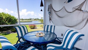 Een ronde glazen tafel met blauw-witte streepstoelen, een hangmat en uitzicht op een meer en begroeiing.