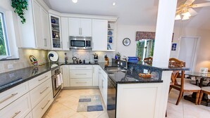 Een moderne keuken met witte kastjes, een inbouwmagnetron en een eethoek met houten stoelen.