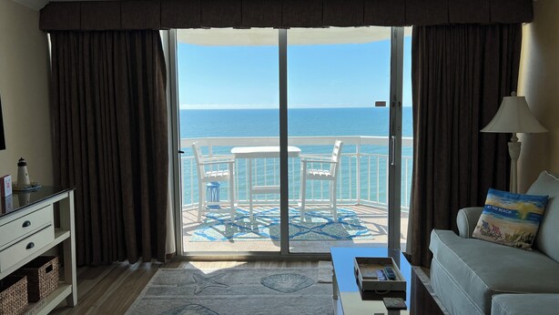 Une chambre d’hôtel avec un balcon, un canapé, une table basse et une vue sur l’océan.
