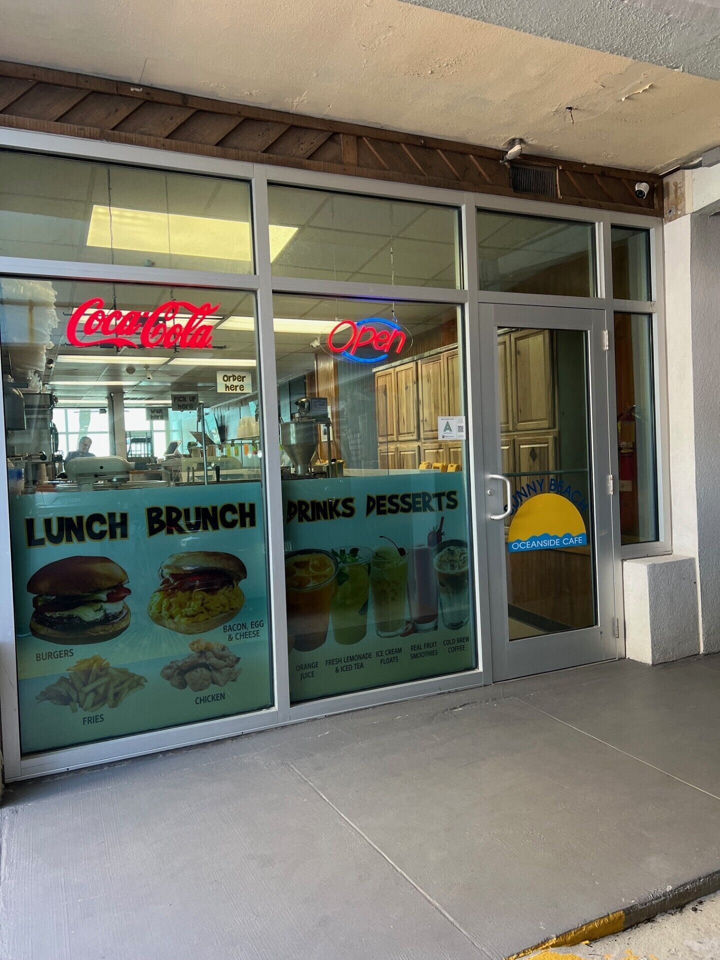 A restaurant with a Coca-Cola sign, an 'Open' sign, and menu boards advertising lunch, brunch, drinks, and desserts.