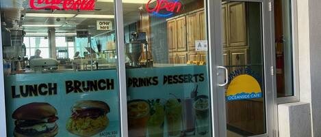 A restaurant with a Coca-Cola sign, an 'Open' sign, and menu boards advertising lunch, brunch, drinks, and desserts.