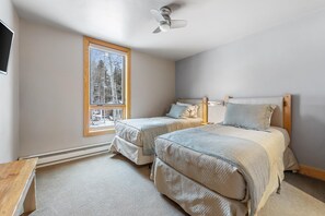 A bedroom with two beds, a ceiling fan, a window with a view of trees, and a wooden nightstand. - Creek‑Side Millrace Three‑Bedroom Retreat (Vail)