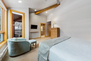 Une chambre à coucher avec un lit, une chaise, une commode, un téléviseur et une fenêtre.