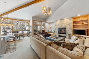 A spacious living room with a large sofa, a fireplace, and a stone accent wall. - Creek‑Side Millrace Three‑Bedroom Retreat (Vail)