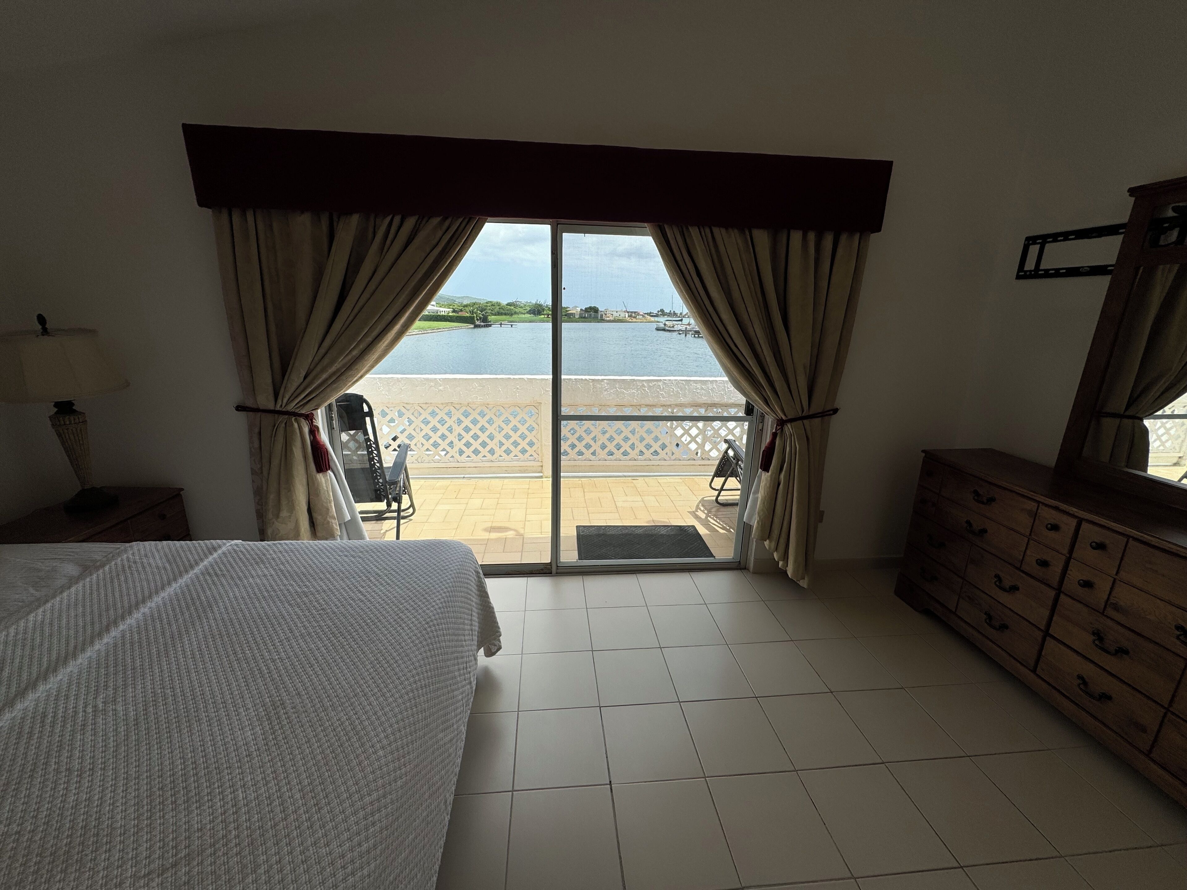 Une chambre d’hôtel avec un lit, une commode, une chaise et une vue sur une étendue d’eau, visible à travers une grande fenêtre.