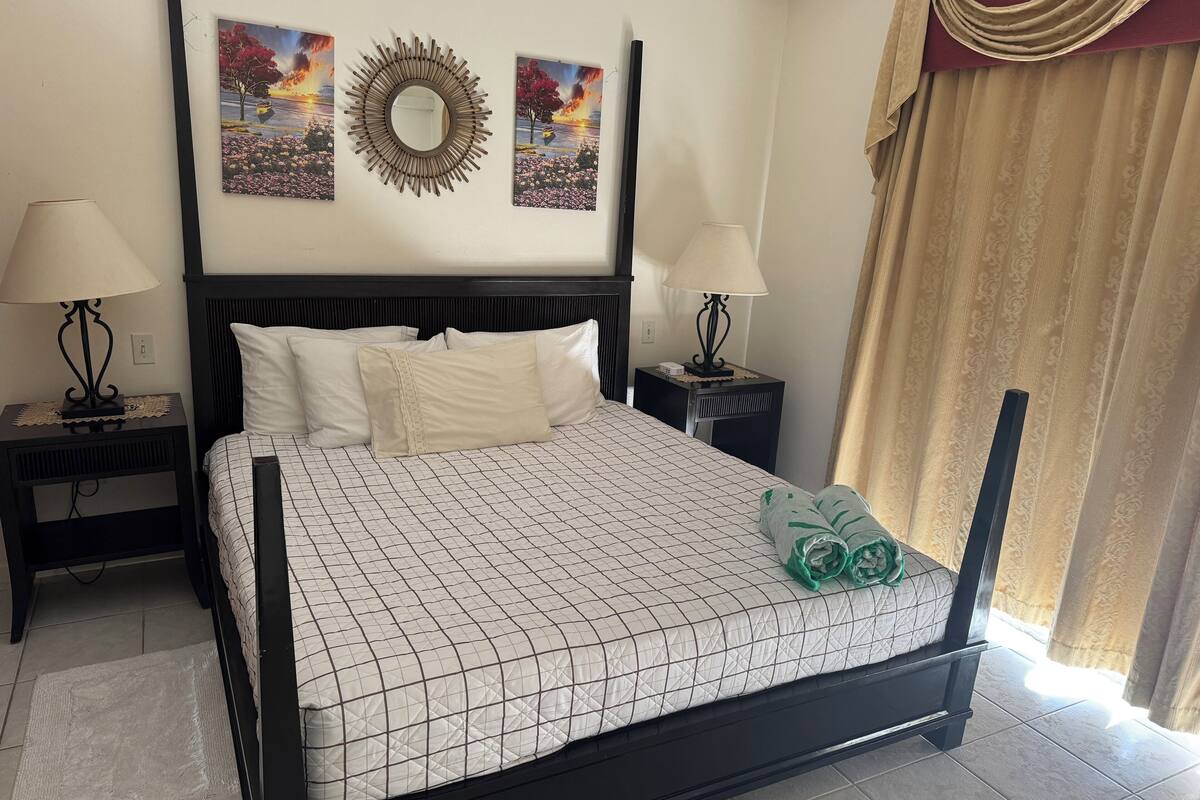 A neatly arranged hotel room with a bed, two bedside tables, two lamps, a mirror, and two wall art pieces.