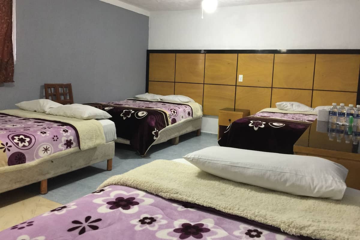 A hotel room with two beds, a wooden headboard, a small table with water bottles, and a chair.