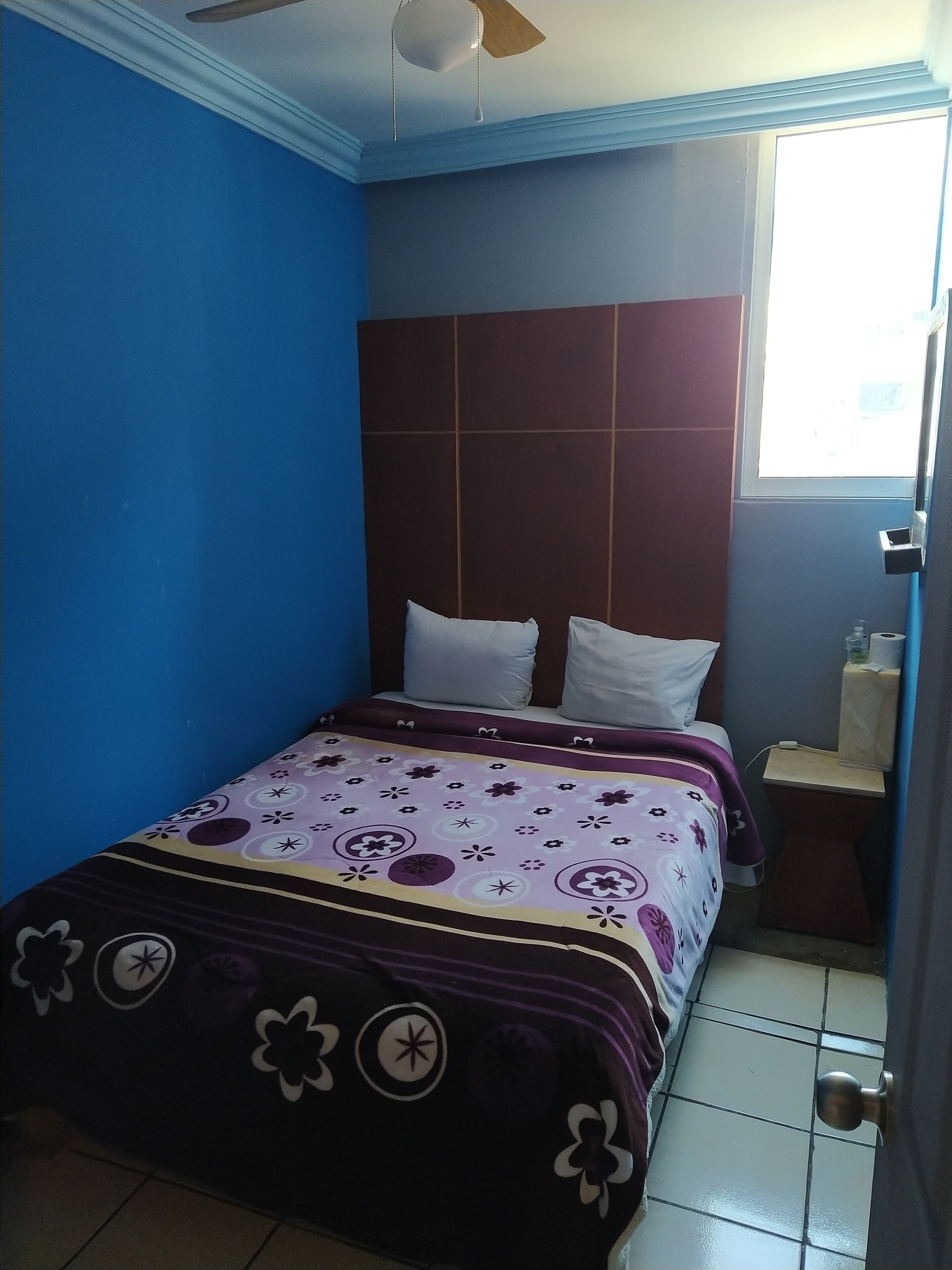 Une chambre à coucher avec un lit, un ventilateur de plafond, une fenêtre et une table de chevet.