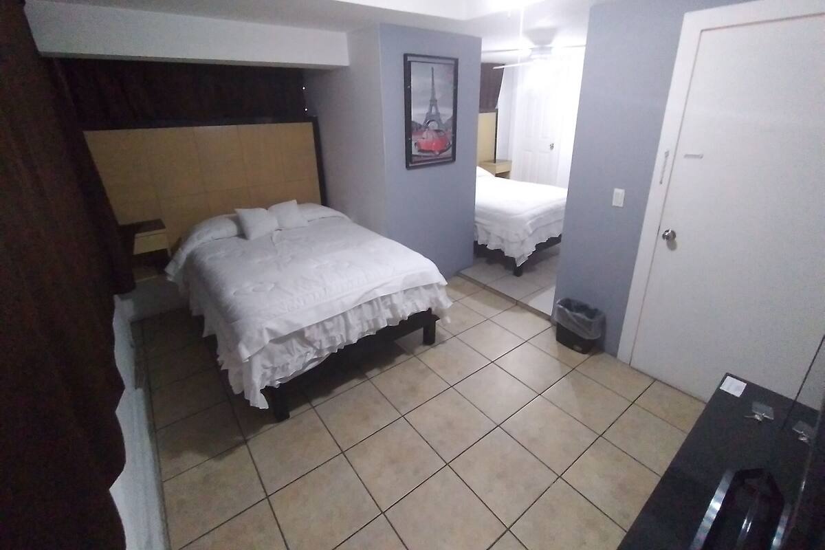 A bedroom with two beds, a ceiling fan, a door, and a trash bin.