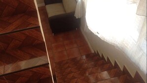 Een kamer met een visgraatvloer, een donkergrijze bank en een raam met witte gordijnen.