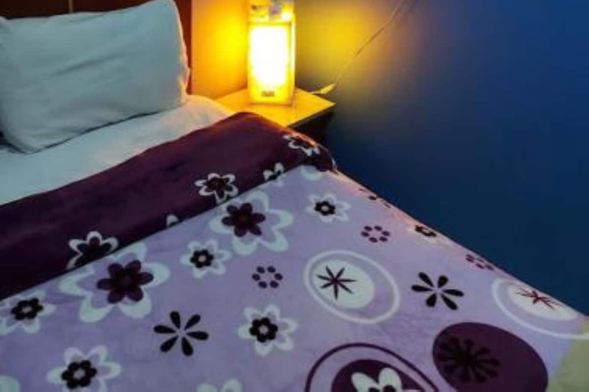 A bedroom with a bed, a nightstand, a lamp, and a wall-mounted mirror.