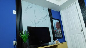 Een kamer met een televisie op een houten dressoir, een wand met een marmerpatroon en een deur met een witte omlijsting.